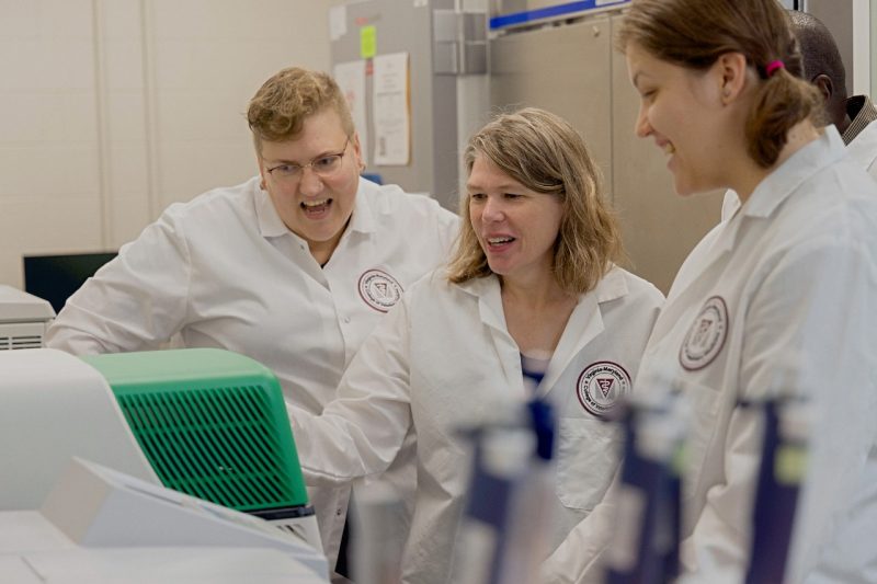 Kirsten Neilsen (at center) surrounded by her lab assistants looking at a machine in their new lab at the Center for One Health Research.