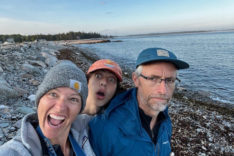 Flori Bliss (at left) standing with two people on an ocean coast. 