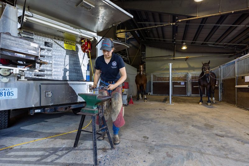 Victoria Protasenko working on a horse shoe beside a farrier truck.